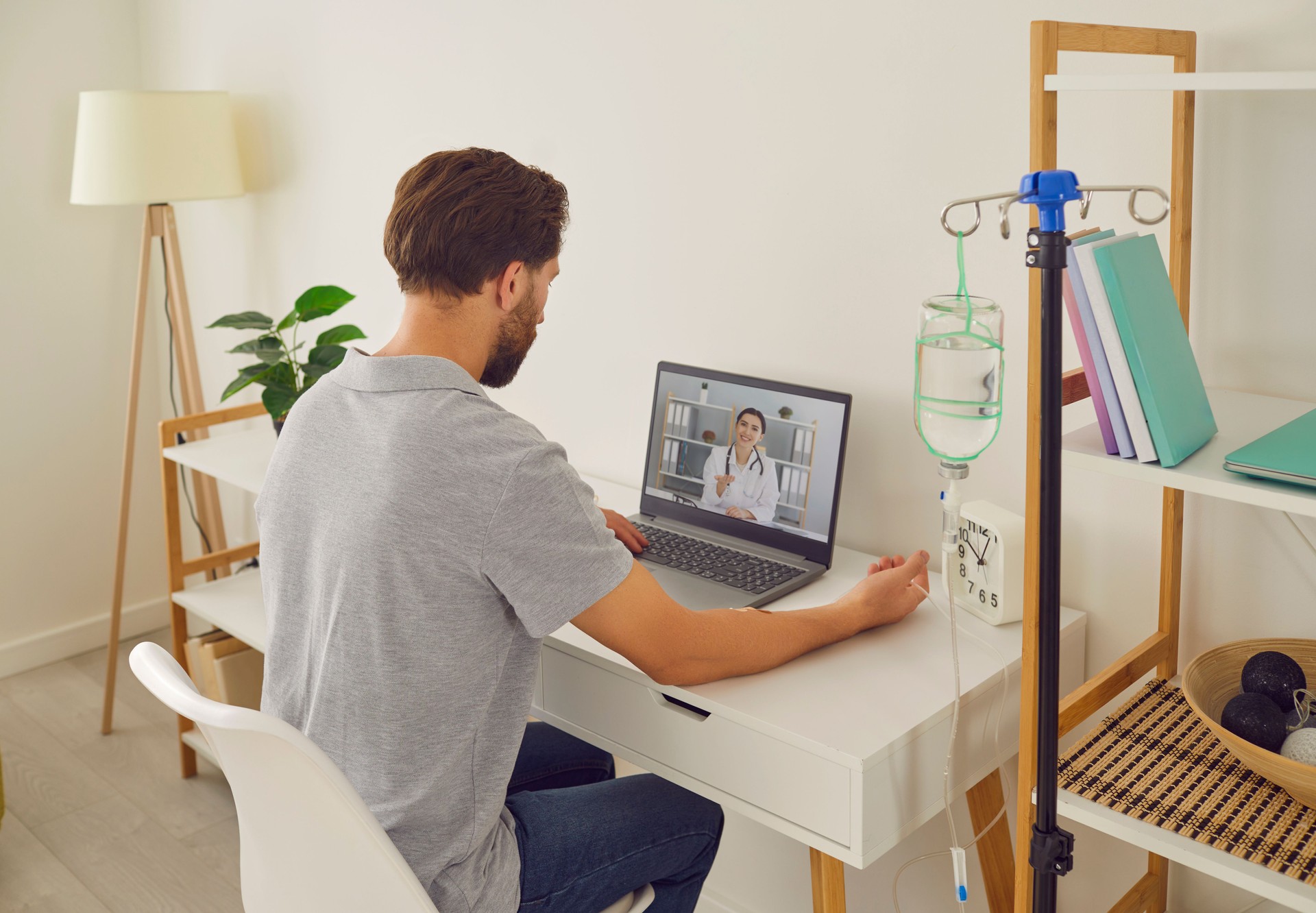 Man having online video call with doctor at home while receiving IV drip infusion